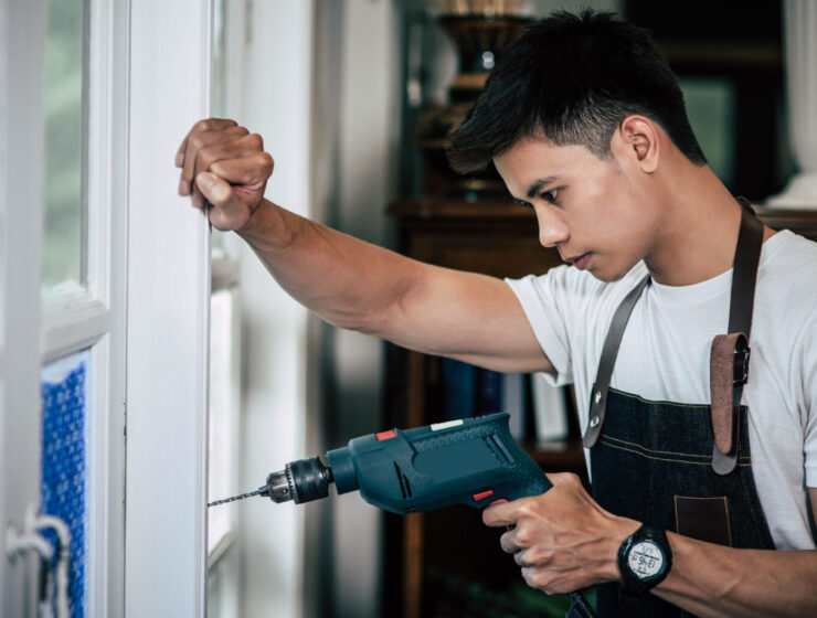 The carpenter holds the drill and drills the window. Selective focus.